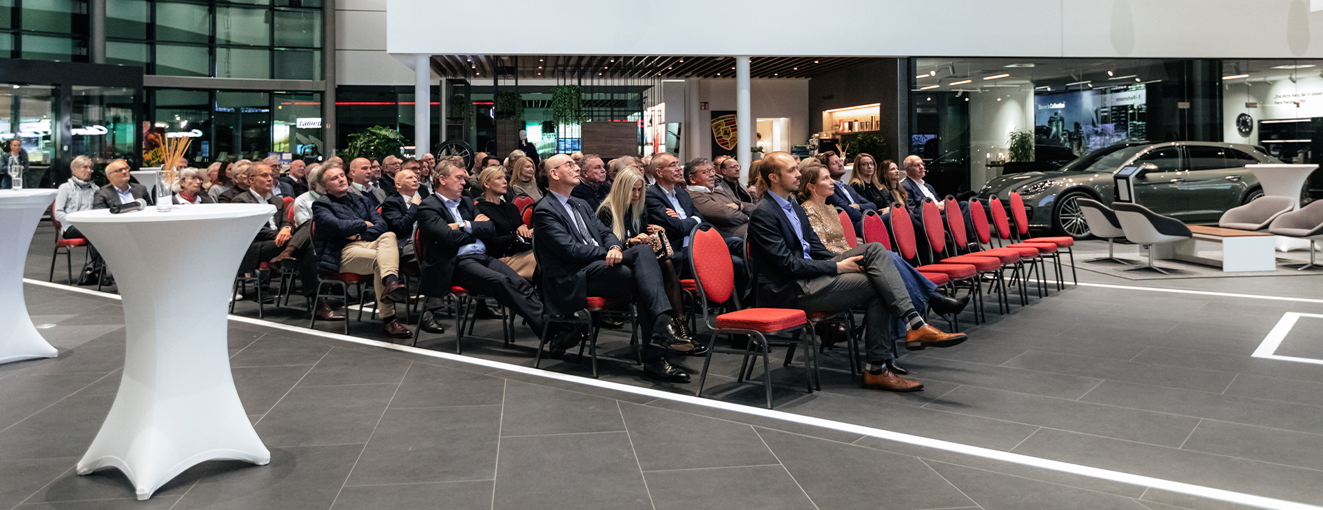 Das Publikum des Porsche Zentrums Augsburg sieht gespannt auf eine Leinwand.